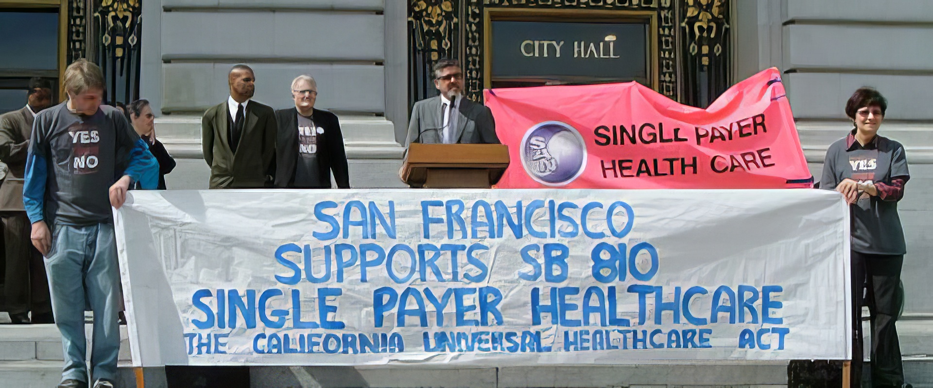 On the steps of SF City Hall, supporters of single payer healthcare hold up a banner that reads "San Francisco supports SB 810 single payer healthcare"